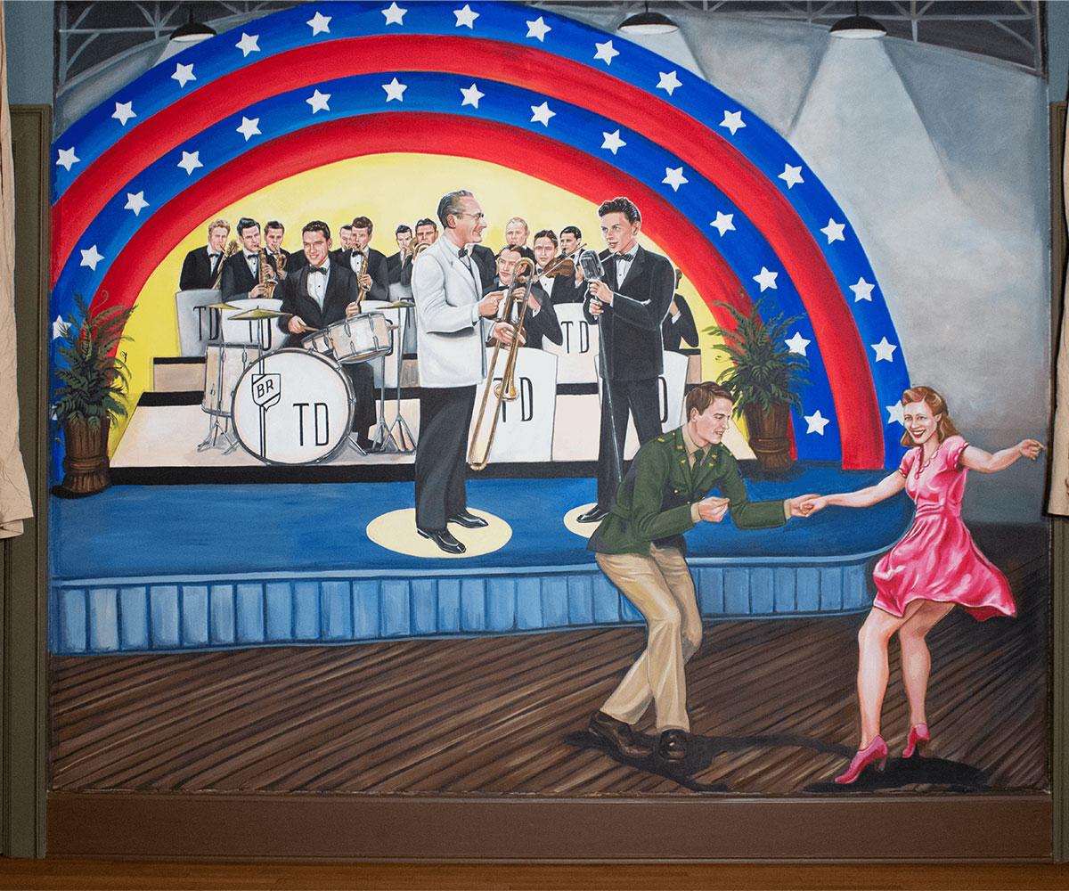 Photo of a mural with early big band orchestra with people dancing in front of it.